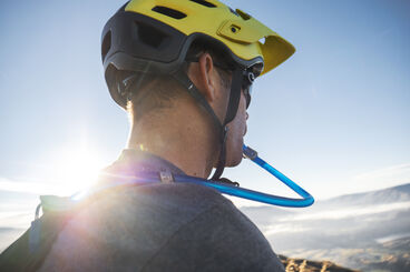 Man in bike helmet drinking water from a hydration pack. 